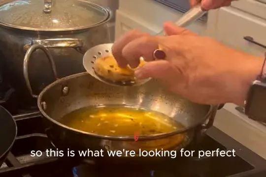 Golden battered eggplant slice lifted from hot oil with a slotted spoon