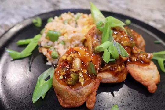 Plated crispy sweet chili eggplant with pea fried rice and spring onions