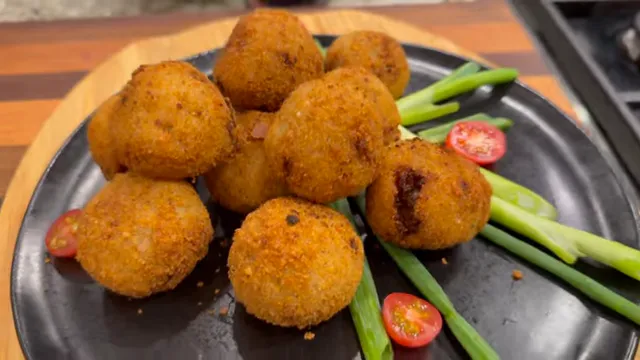 Golden fried vegan keema rice balls on a black platter with green onions and halved cherry tomatoes