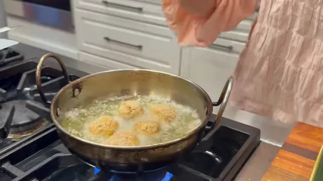 Five breadcrumb-coated rice balls frying in bubbling oil in a metal pan