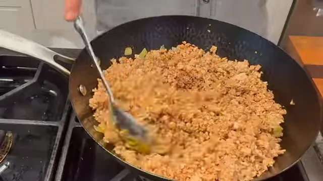 Hydrated TVP being stirred into browned onions and whole spices in a black wok