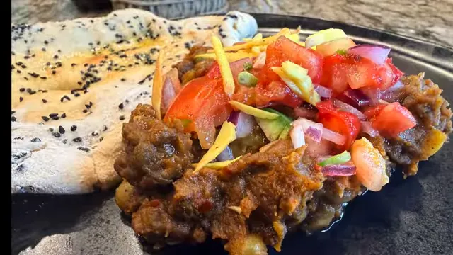 Spiced pea curry topped with tomatoes onion and ginger beside nigella seed kulcha