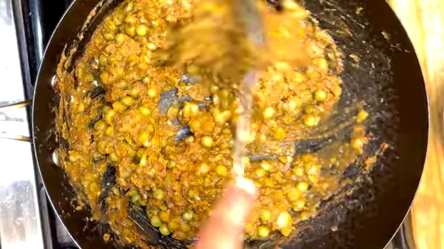 Thick spiced pea curry being stirred in a black pan