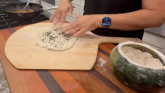 Flattened kulcha dough covered with nigella seeds on a wooden board