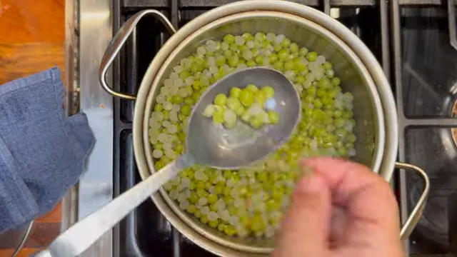 Cooked green peas in a spoon over a pot