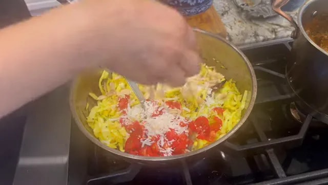 Tomatoes, shredded coconut, and sliced almonds added on top of yellow cooked cabbage in a skillet