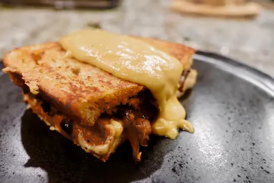 Crispy grilled mushroom sandwich topped with creamy yellow vegan cheese sauce