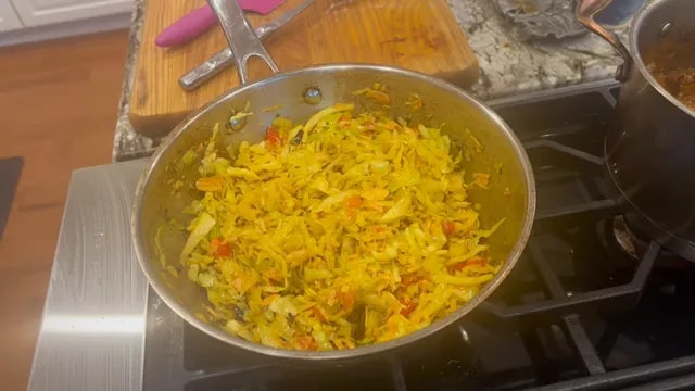 Finished golden cabbage salad with red tomato pieces and nutty topping in a skillet