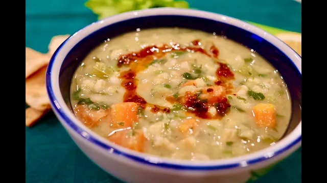 Bowl of creamy pea soup with carrots, green herbs, and a swirl of red sauce
