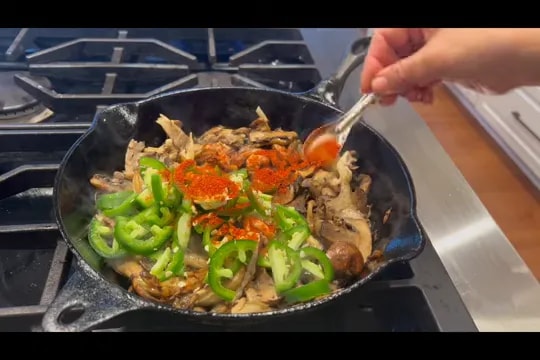 Cast iron skillet filled with mushrooms, green peppers, and red spices