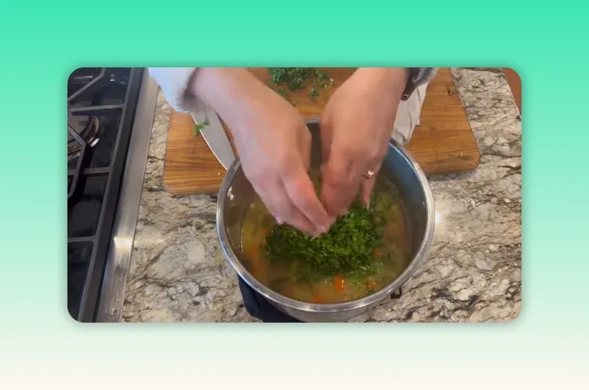 A large mound of chopped parsley added to creamy pea soup in a metal pot
