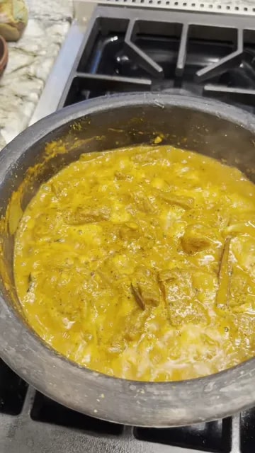 Golden yellow curry with onion slices and wheat gluten pieces simmering in a black pan