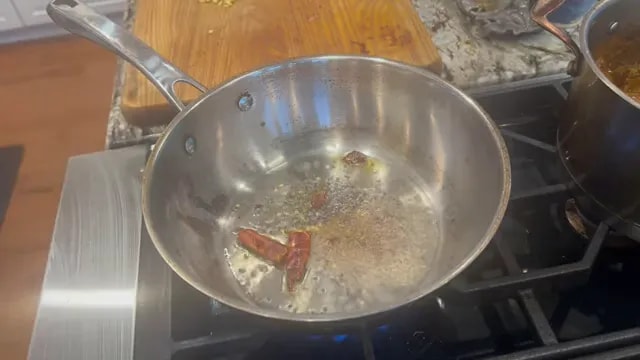 Dried red chili and whole spices sizzling in oil in a stainless steel skillet