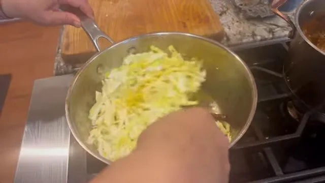 Shredded cabbage coated in yellow turmeric spices being stirred in a skillet