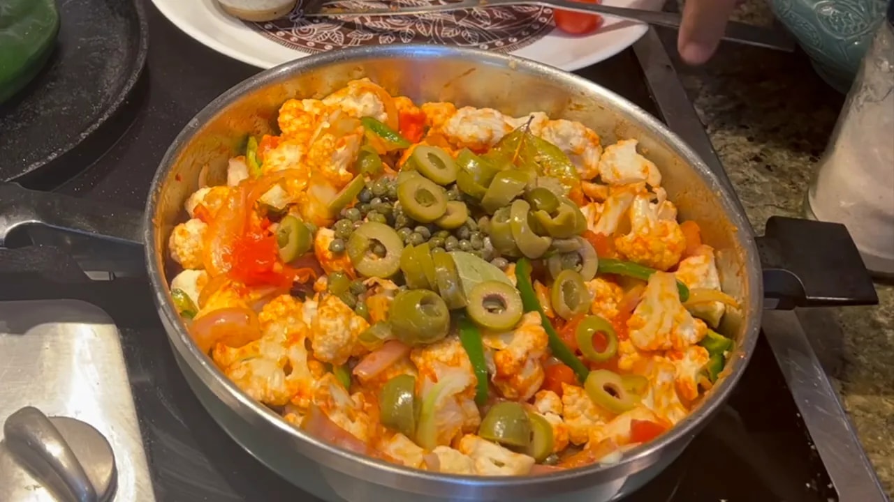 Sliced green olives and capers on top of cauliflower, tomatoes, onions, and green peppers in a skillet