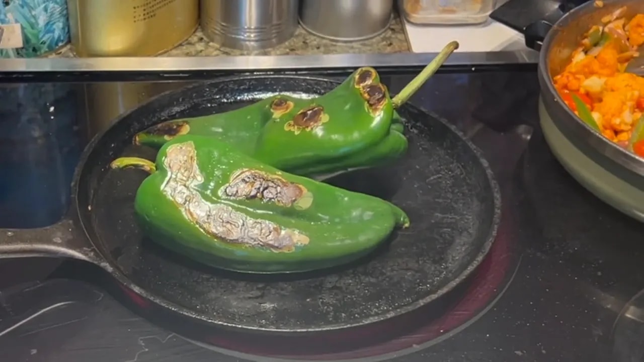 Two green poblano peppers with blistered brown and black patches in a cast iron pan
