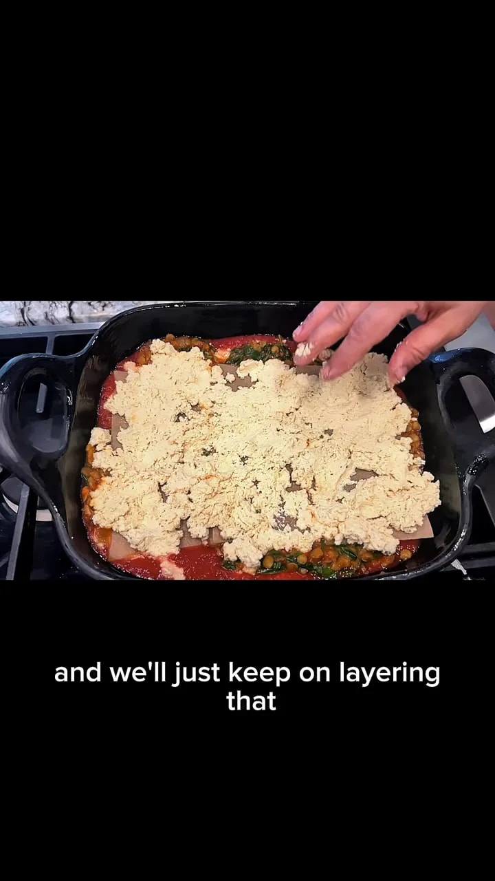 Lasagna pan with a pale crumbly ricotta layer and tomato sauce and greens visible around the edges
