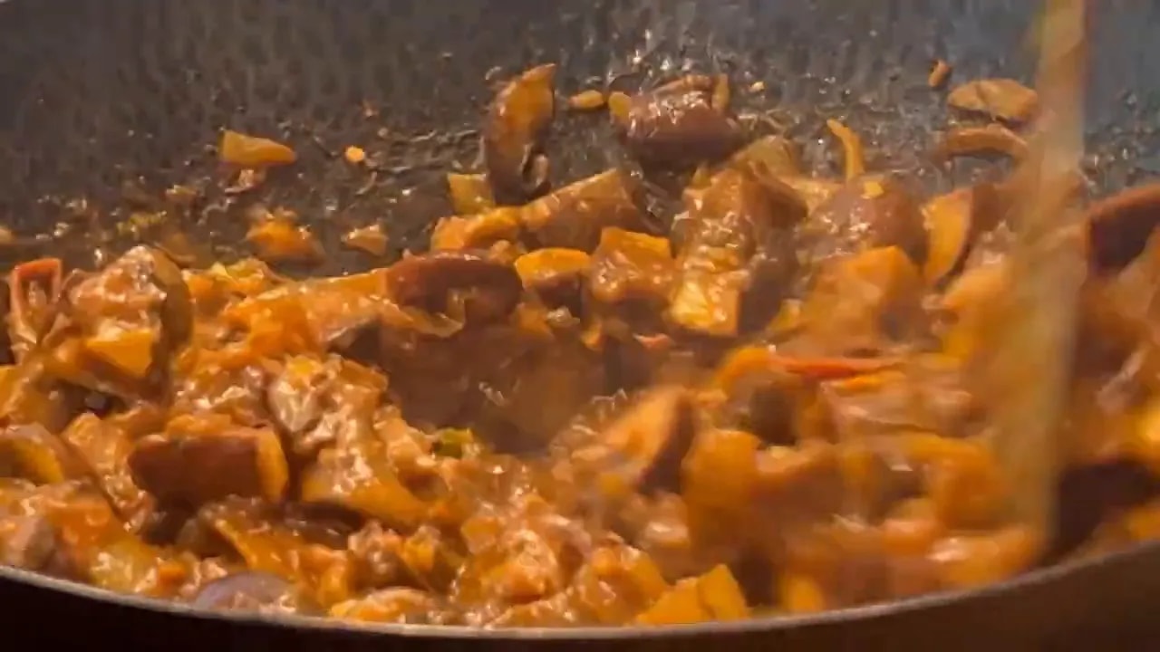 Close-up of mushrooms and softened onions coated in thick reddish-brown masala inside a wok