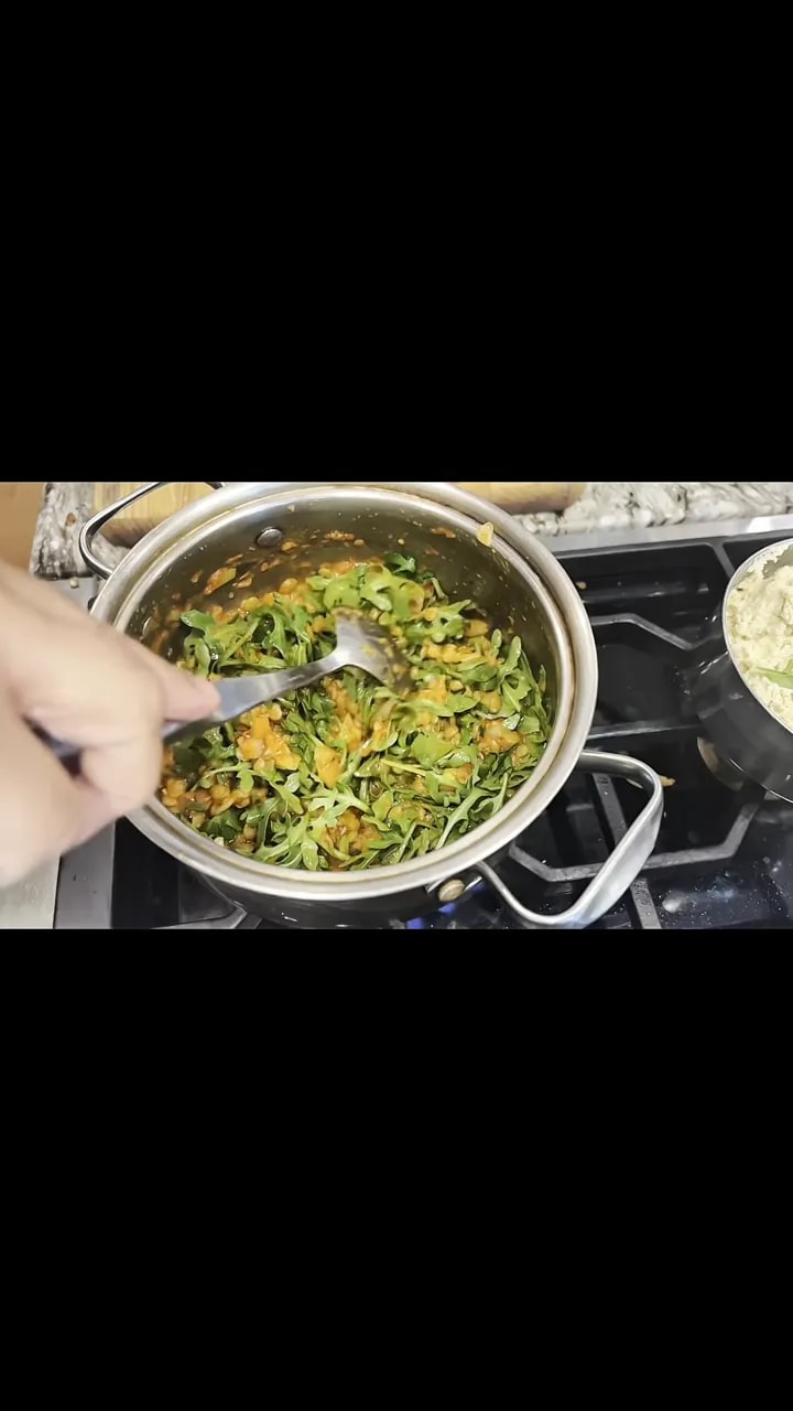 Green leaves mixed with lentils and tomato sauce in a stainless-steel pot