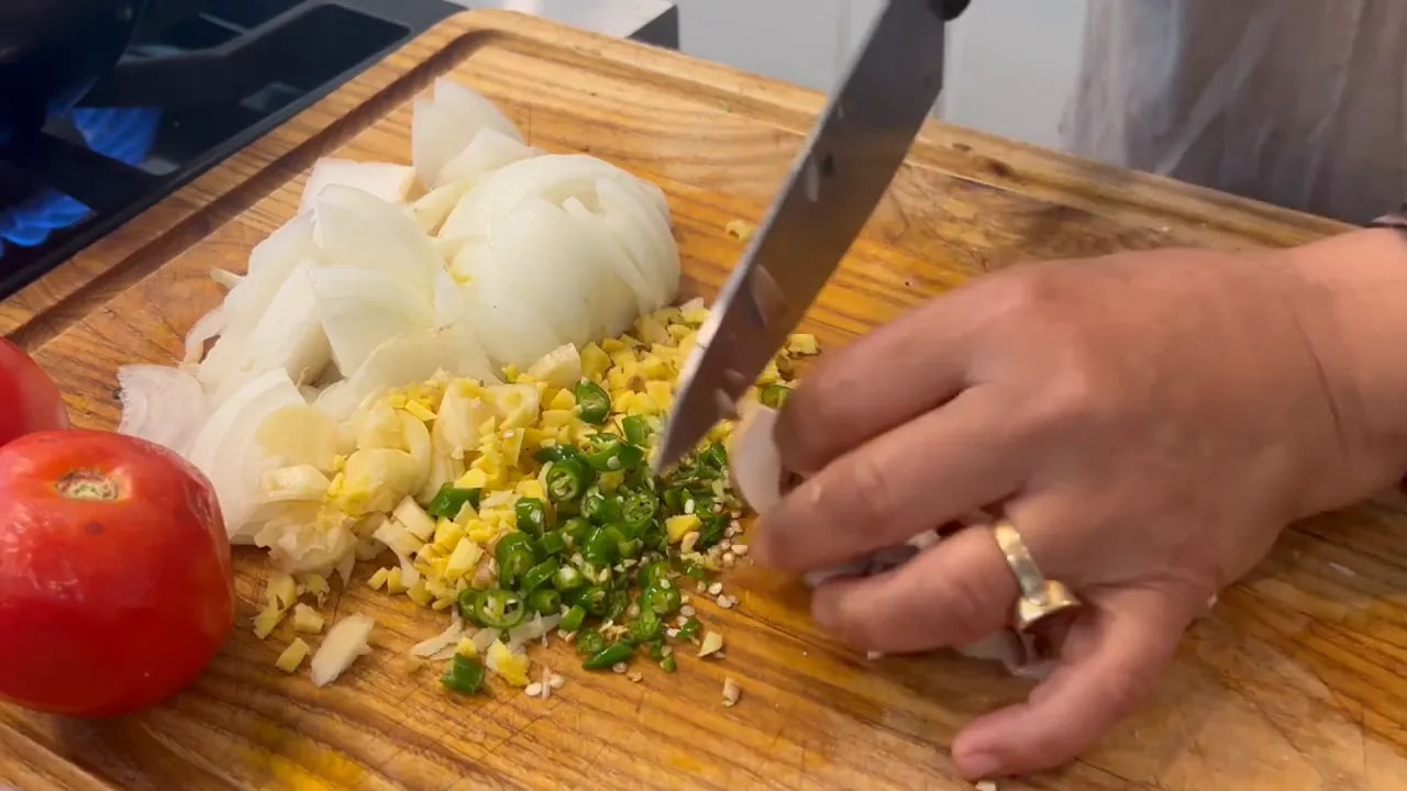 Roughly chopped mushrooms beside chopped onion, garlic, ginger, and green chilies on a wooden board