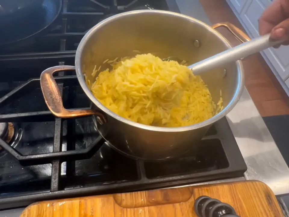 Spoon lifting long yellow basmati grains above a pot of saffron rice