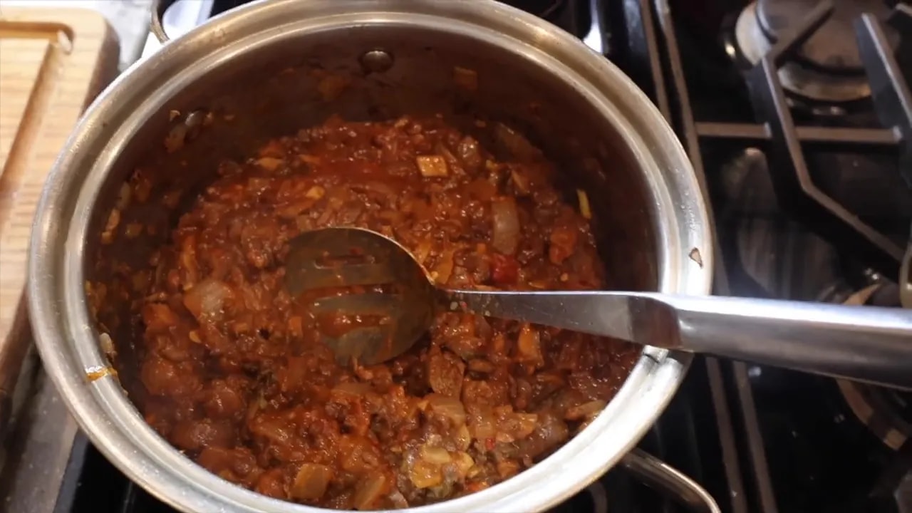 Thick red tomato sauce with visible lentils and mushroom pieces in a stainless steel pot