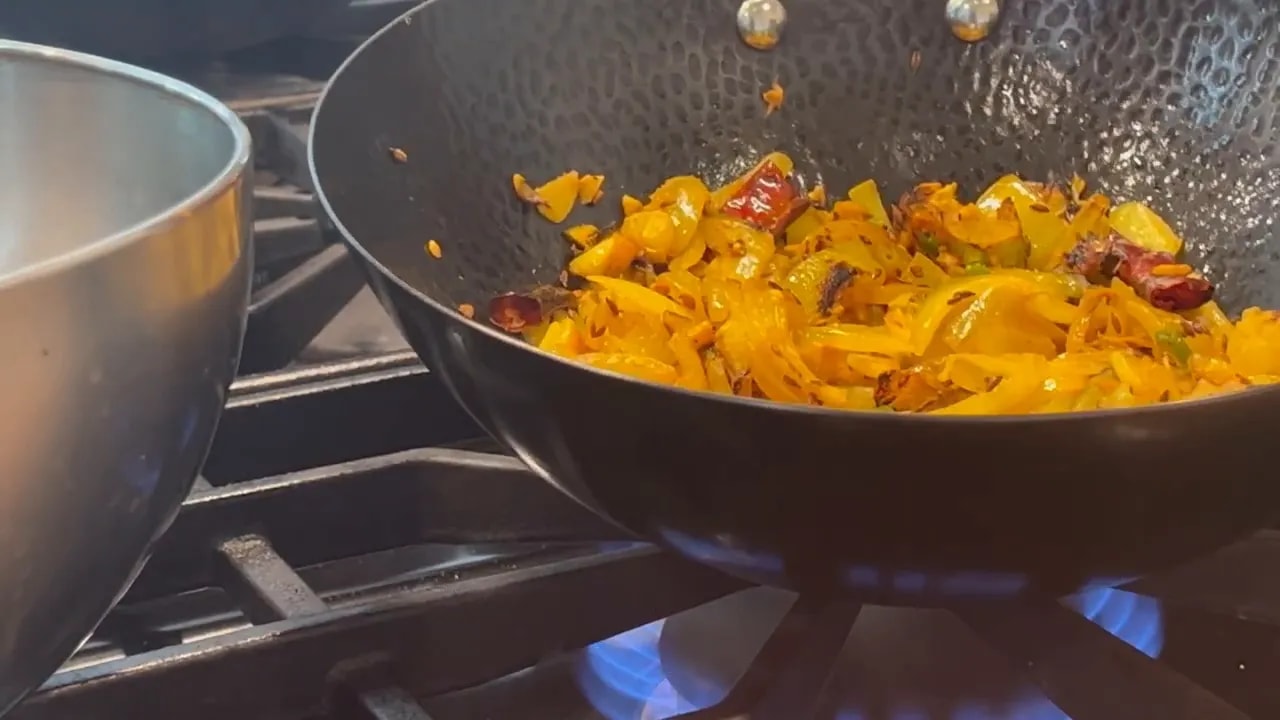 Softened yellow onions with whole dried red chilies and spices in a black wok
