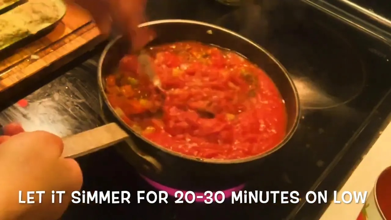 Chunky red tomato sauce being stirred in a saucepan with text instructing a low simmer for 20 to 30 minutes